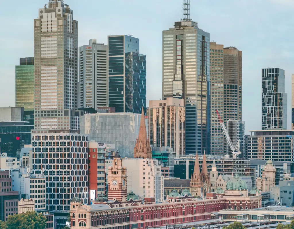 Cityscape of Melbourne, Australia, featuring modern skyscrapers, historic buildings, and Flinders Street Station in the foreground.